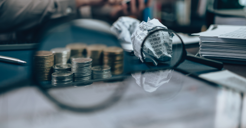 Vergrootglas vergroot een stapel munten en een prop paier met allerlei kosten erop